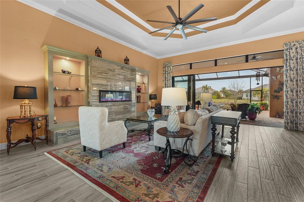 A living room features a fireplace, built-in shelving, a ceiling fan, and large sliding glass doors — 12012 LEGACY ESTATES BOULEVARD, SARASOTA, FL