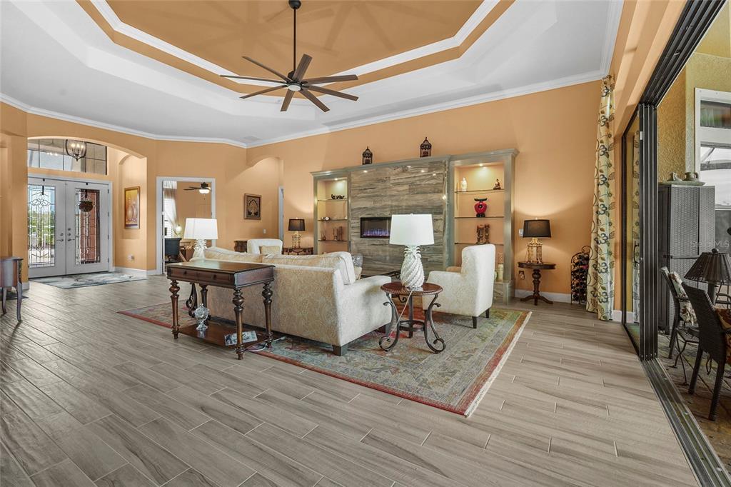 A spacious living room features a tray ceiling, tile flooring, and a stone fireplace wall — 12012 LEGACY ESTATES BOULEVARD, SARASOTA, FL