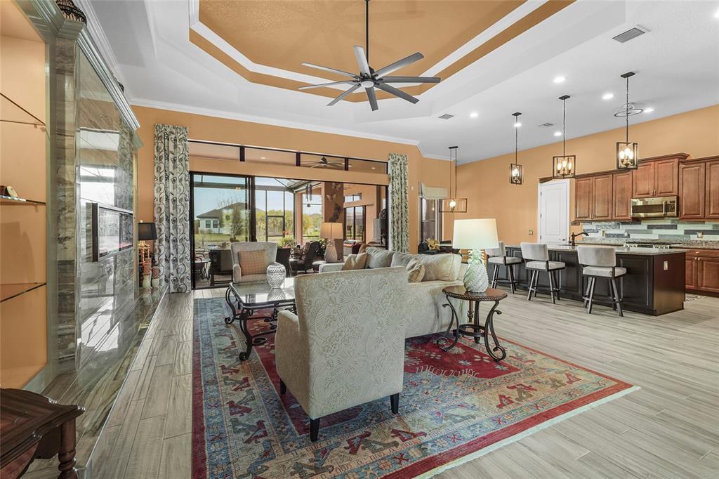 An open-concept living room and kitchen featuring a tray ceiling, fireplace, and sliding glass doors — 12012 LEGACY ESTATES BOULEVARD, SARASOTA, FL