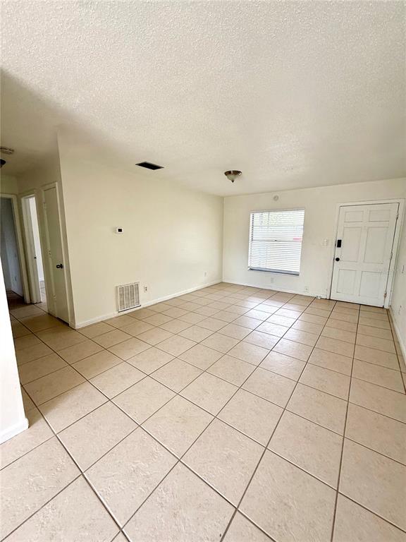 An empty living room features beige tile flooring, white walls, and a white front door — 2800 E 113TH AVENUE UNIT B4, TAMPA, FL