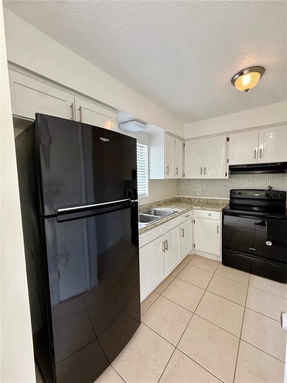 A kitchen features white cabinets, black appliances, and light-colored tile flooring — 2800 E 113TH AVENUE UNIT B4, TAMPA, FL
