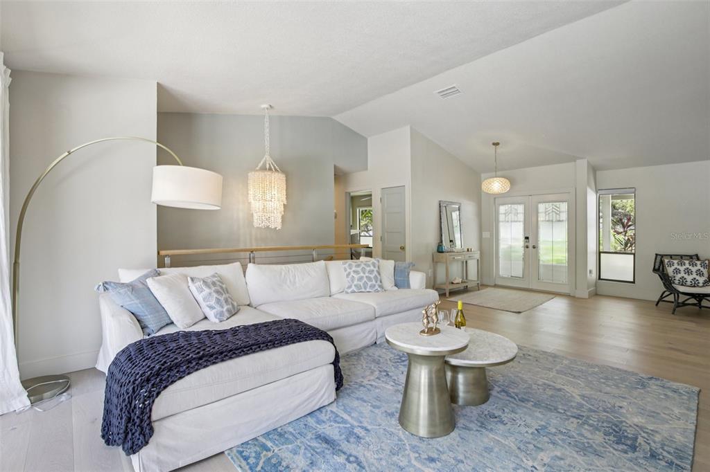 A bright living room features a white sectional sofa, blue area rug, and vaulted ceilings — 3390 BAYOU SOUND, LONGBOAT KEY, FL
