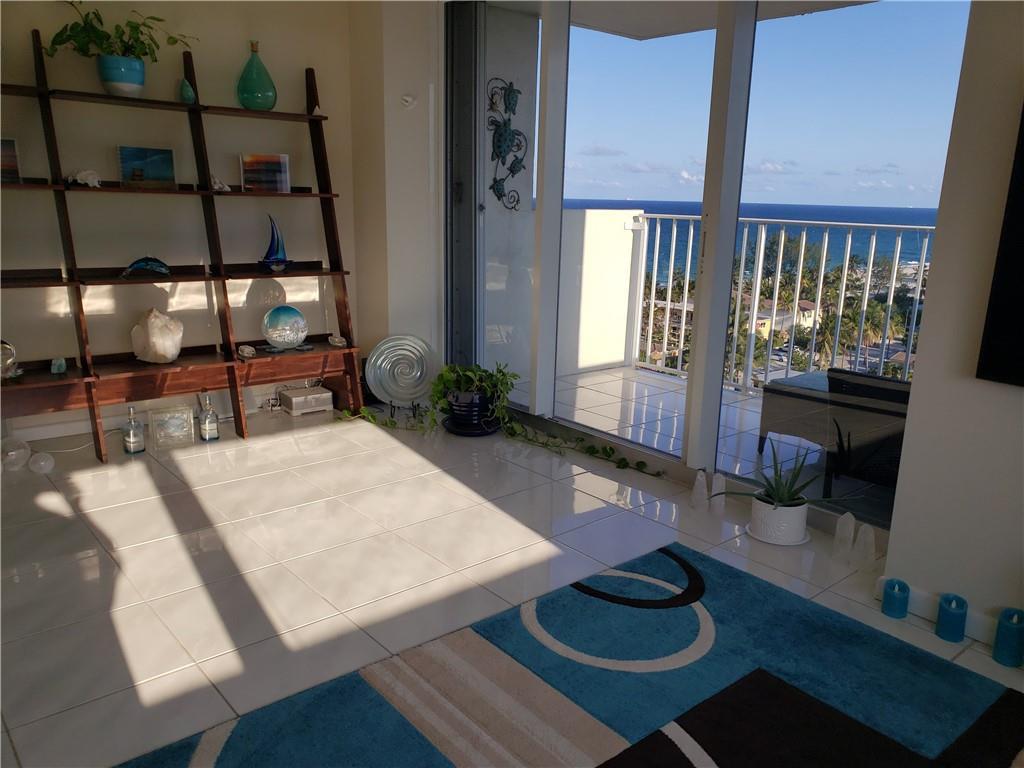 A living room with a wooden shelving unit, tile floors, and a balcony overlooking the ocean — 111 Briny Avenue # 1214, Pompano Beach FL 33062, POMPANO BEACH, FL