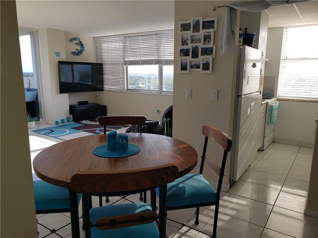 A dining area with a round wooden table sits adjacent to a kitchen and living room — 111 Briny Avenue # 1214, Pompano Beach FL 33062, POMPANO BEACH, FL