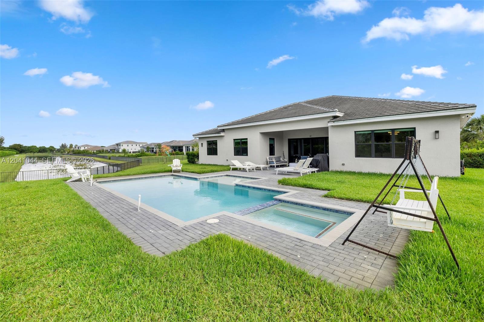 A backyard features a swimming pool, a spa, a white swing, and a patio — 14850 Millstone Ranches Dr, Davie FL 33331, DAVIE, FL
