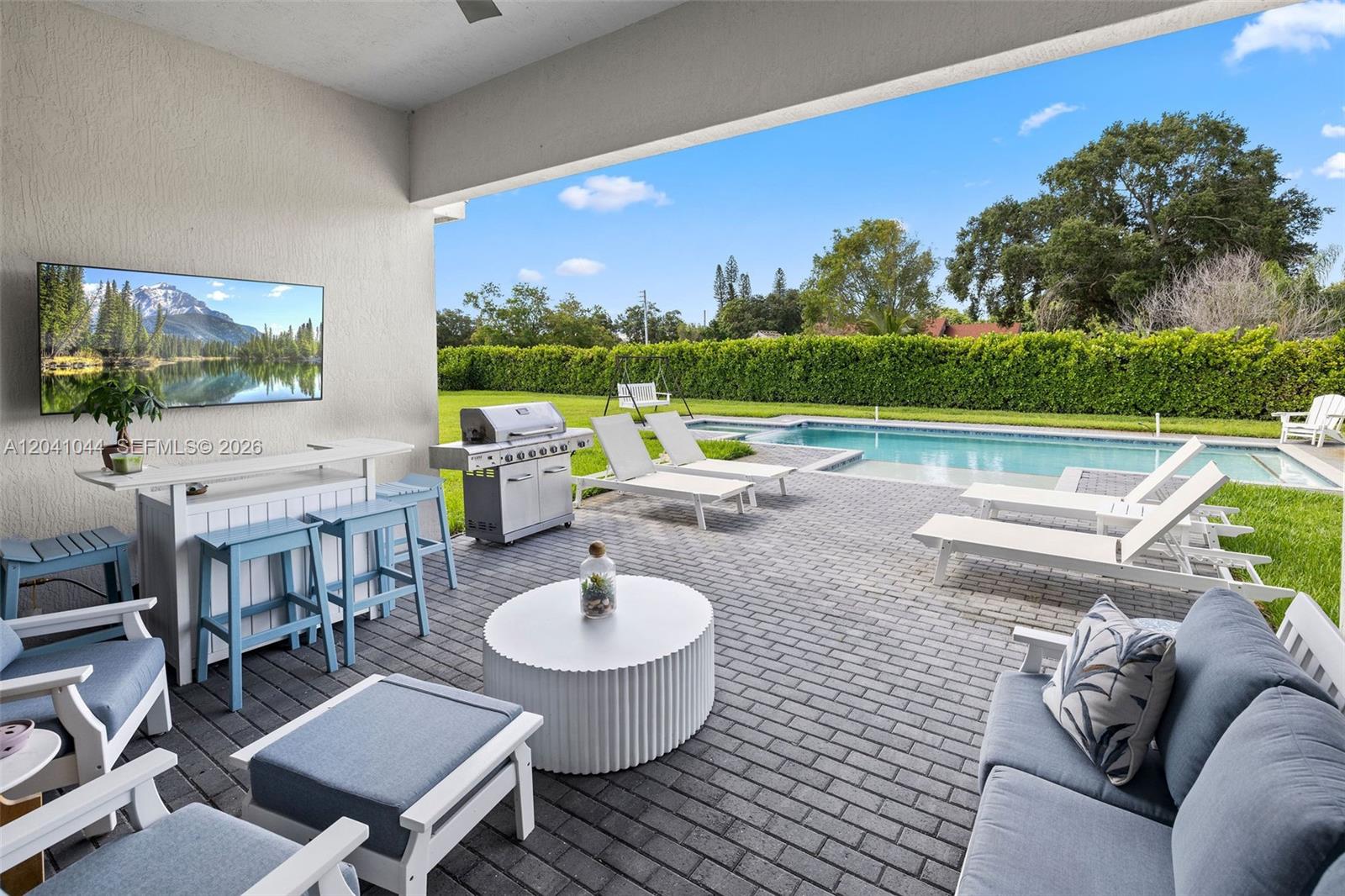 A covered patio features a bar, grill, lounge seating, and a pool in the backyard — 14850 Millstone Ranches Dr, Davie FL 33331, DAVIE, FL