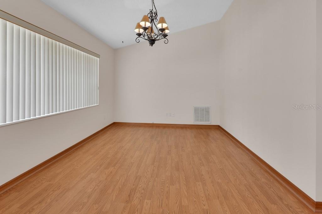 An empty room with light wood-look flooring, beige walls, a chandelier, and vertical window blinds — 750 OAK TERRACE, ORANGE CITY, FL