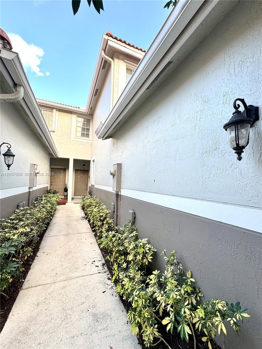 A concrete walkway leads between two stucco buildings with exterior wall lanterns and landscaping — 3742 San Simeon Cir # 3742, Weston FL 33331, WESTON, FL