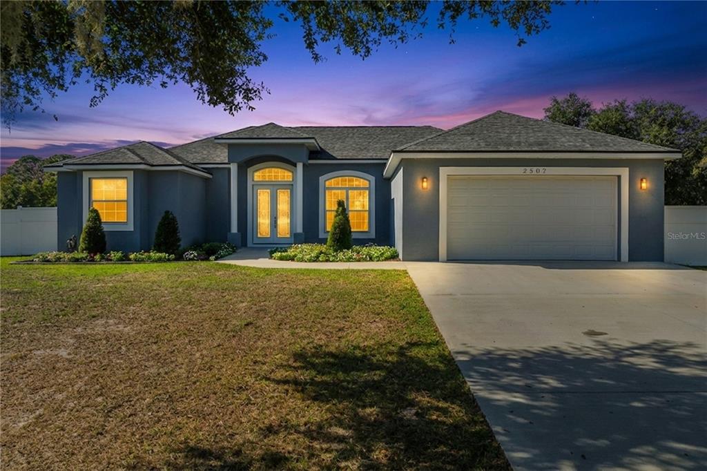 A single-story blue house with a two-car garage and a paved driveway at dusk — 2502 LAKE FRONT DRIVE, LAKE WALES, FL