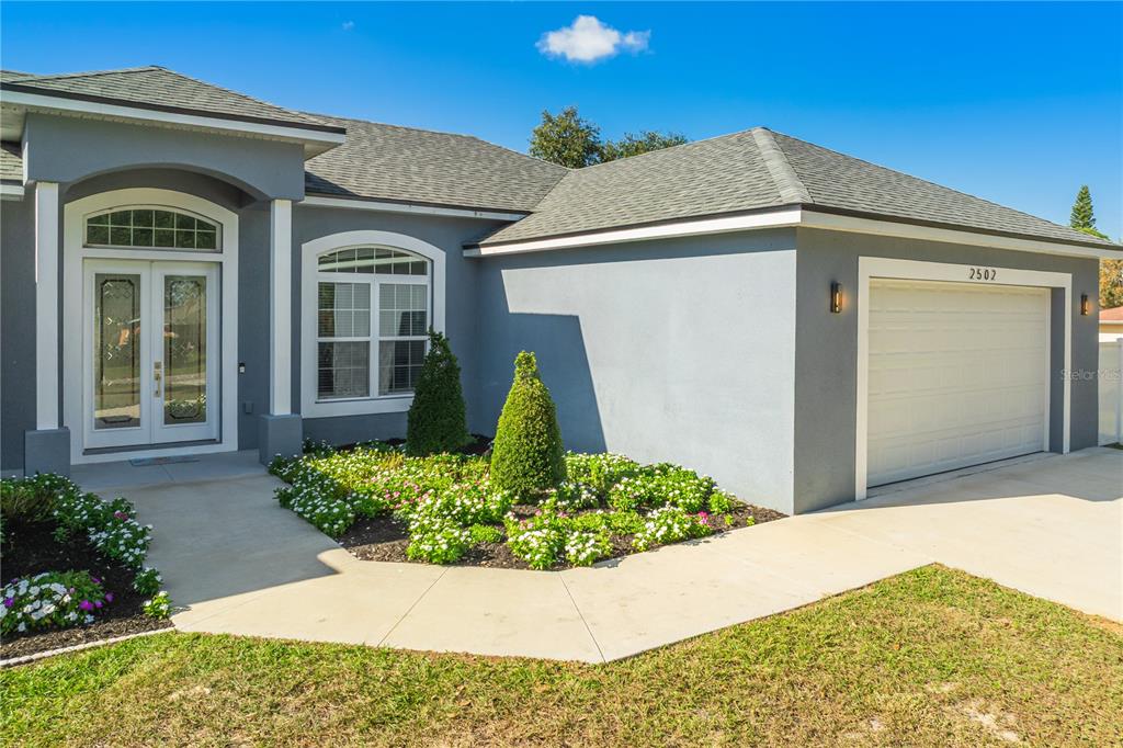 A single-story house exterior with a gray stucco facade, double front doors, and a garage — 2502 LAKE FRONT DRIVE, LAKE WALES, FL