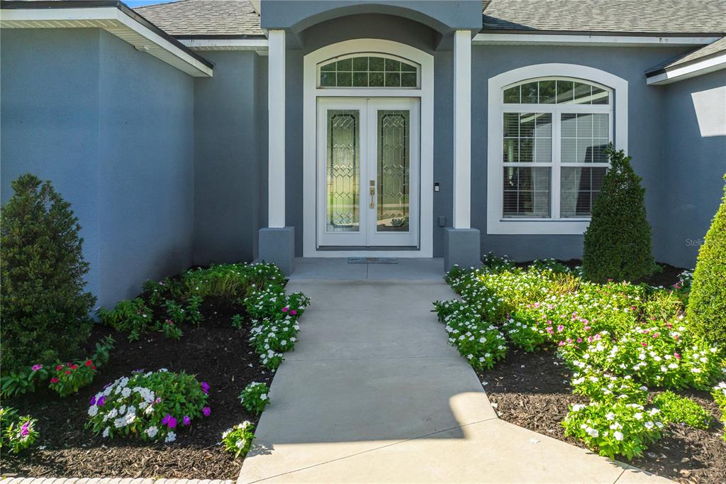 The front entrance of a house features double glass doors, white columns, and flower beds — 2502 LAKE FRONT DRIVE, LAKE WALES, FL