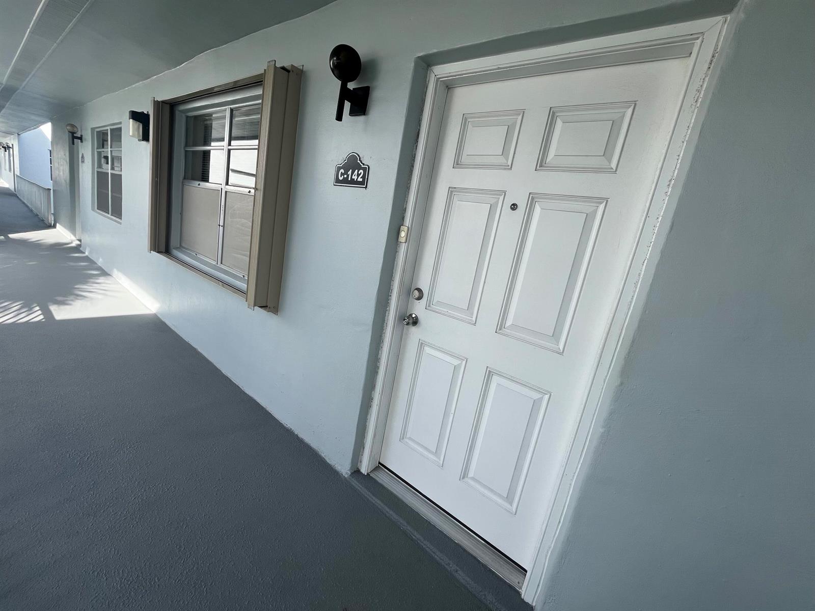 An exterior view of a white apartment door labeled C-142 with a nearby window — 142 Normandy C, Delray Beach FL 33484, DELRAY BEACH, FL