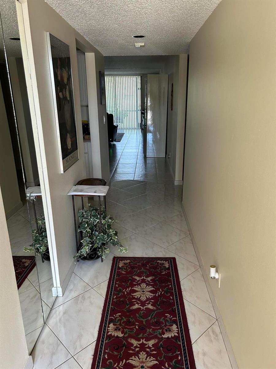 A hallway with light-colored tile flooring, a red runner rug, and a large wall mirror — 4725 Lucerne Lakes Boulevard # 115, FL 33467, FL