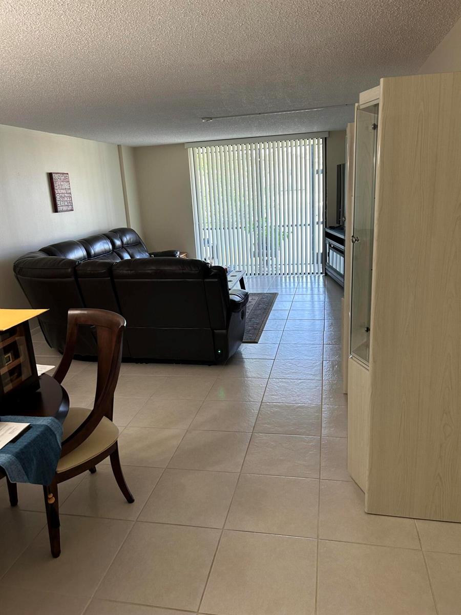 A living room with tile flooring, a dark leather sofa, and vertical blinds on a window — 4725 Lucerne Lakes Boulevard # 115, FL 33467, FL