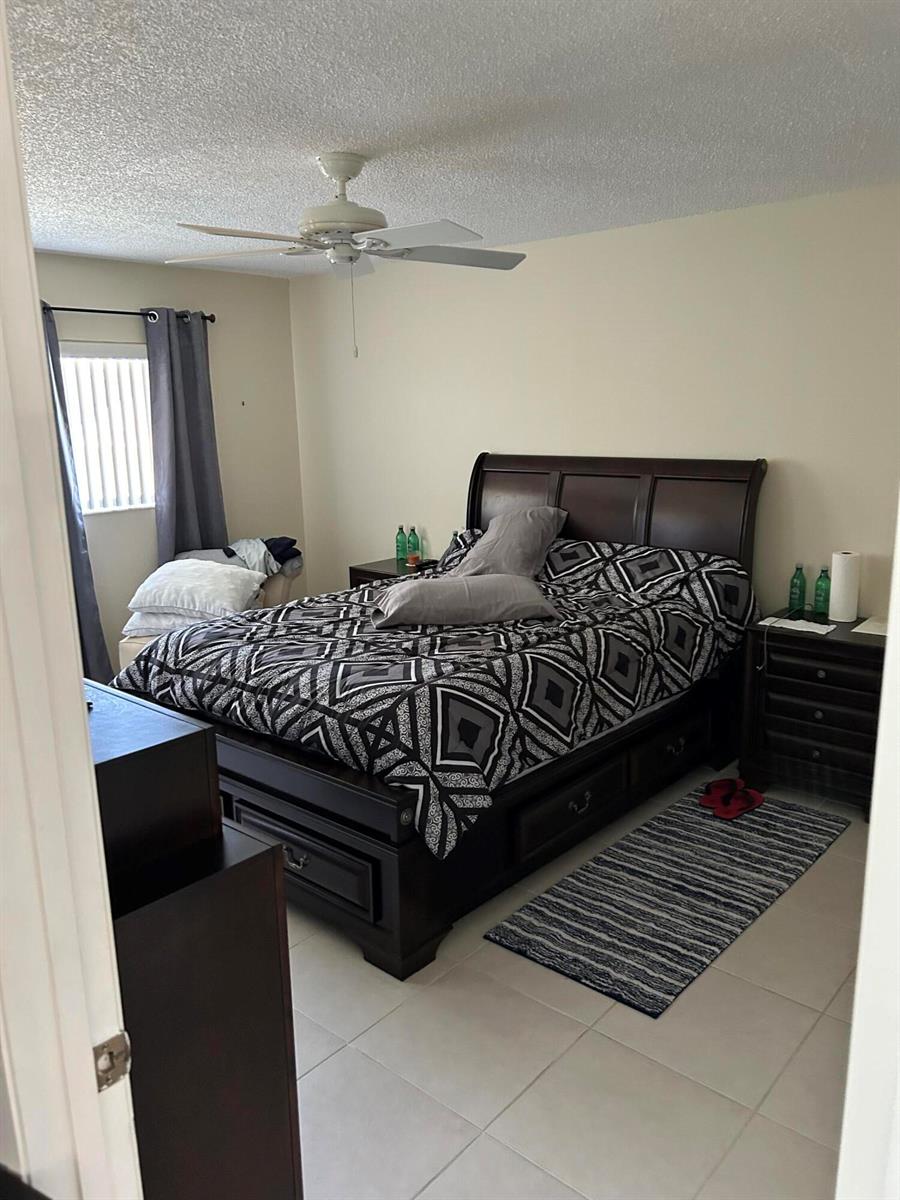 A bedroom features a dark wood sleigh bed, tile flooring, and a ceiling fan — 4725 Lucerne Lakes Boulevard # 115, FL 33467, FL