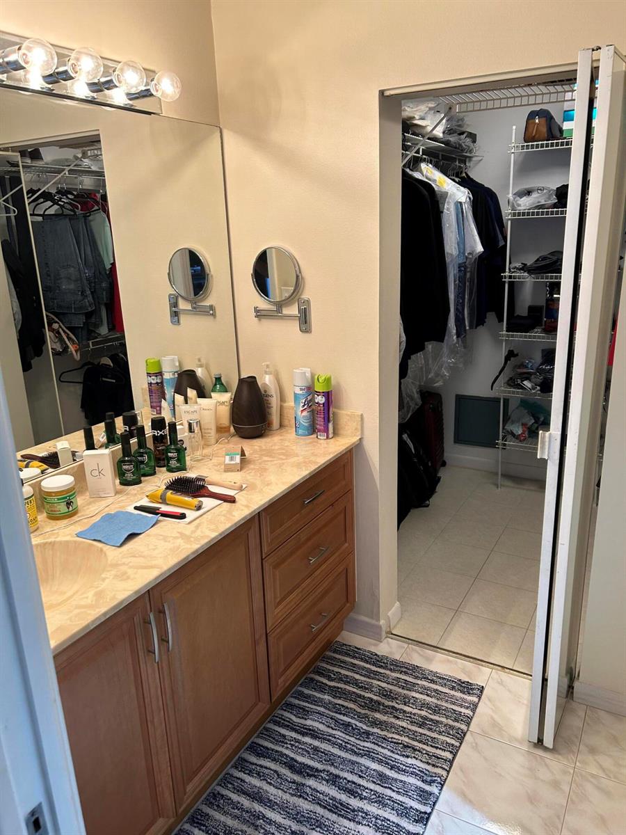 A bathroom vanity with wood cabinets and a marble countertop next to a walk-in closet — 4725 Lucerne Lakes Boulevard # 115, FL 33467, FL