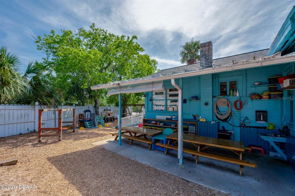 A backyard features a blue house exterior, a covered patio with picnic tables, and playground equipment — 510 DUNLAWTON AVENUE, PORT ORANGE, FL