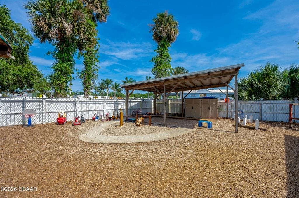 An outdoor playground area features a covered structure, wood chip ground, and a white fence — 510 DUNLAWTON AVENUE, PORT ORANGE, FL