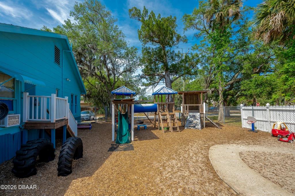A backyard playground with wooden structures and a slide sits beside a blue house — 510 DUNLAWTON AVENUE, PORT ORANGE, FL