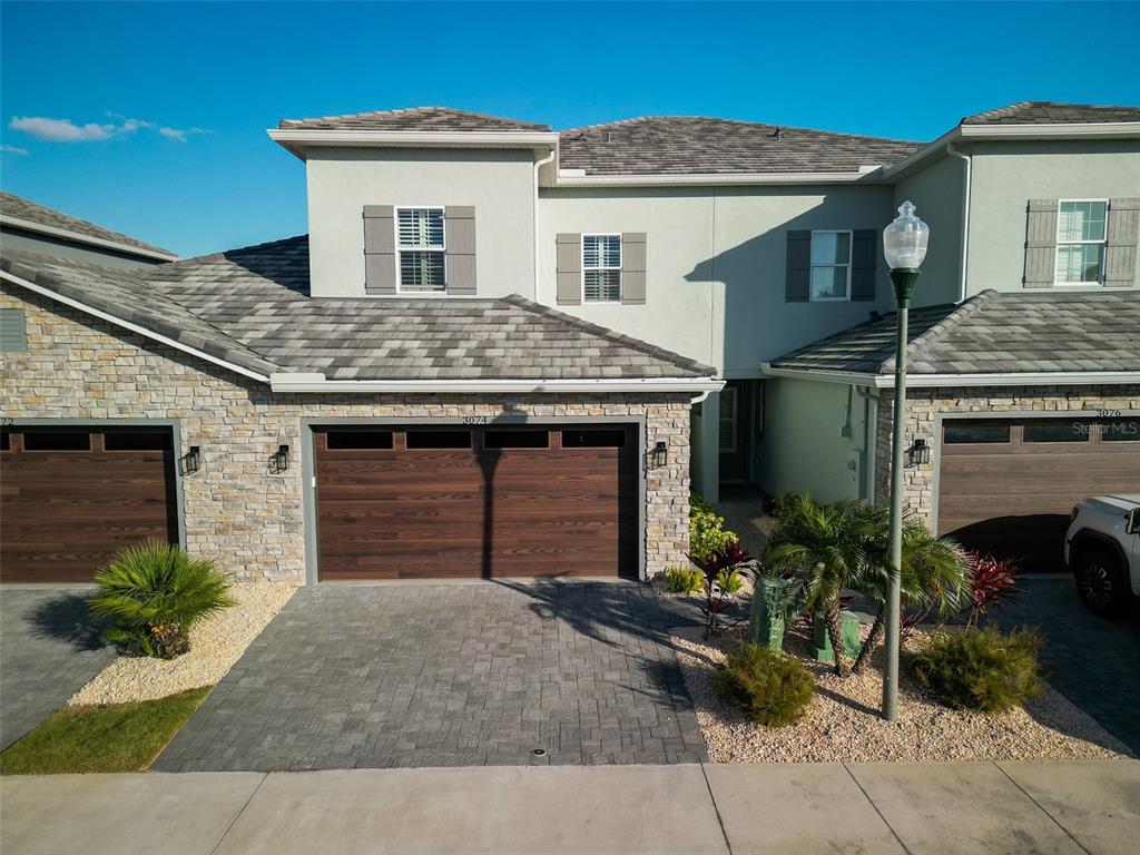 A two-story townhouse with a stone facade, a wooden garage door, and a paved driveway — 3074 ISLES WAY, NEW SMYRNA BEACH, FL