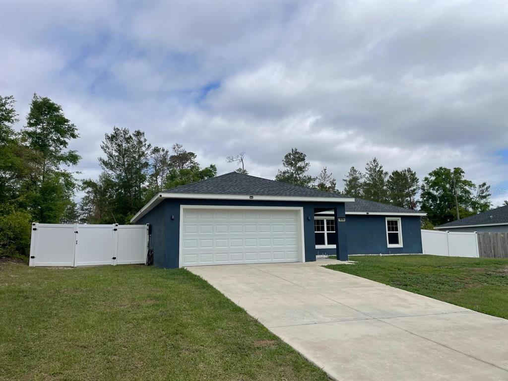 A blue single-story house with a white garage door, concrete driveway, and white vinyl fencing — 16958 SW 20TH COURT ROAD, OCALA, FL
