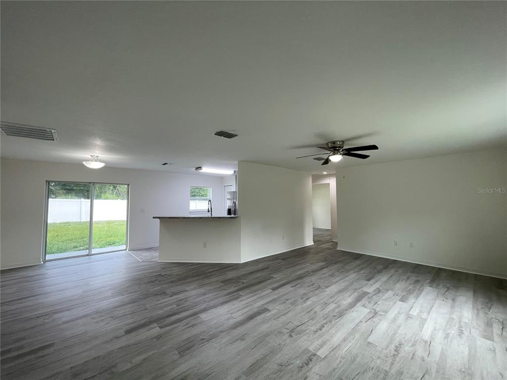 An open-concept living area features gray wood-look flooring, a ceiling fan, and a kitchen peninsula — 16958 SW 20TH COURT ROAD, OCALA, FL