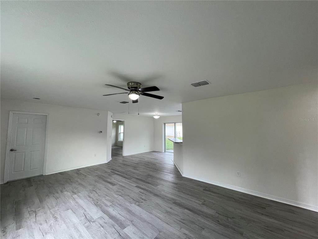 An open-concept living area features light gray wood-look flooring, white walls, and a ceiling fan — 16958 SW 20TH COURT ROAD, OCALA, FL