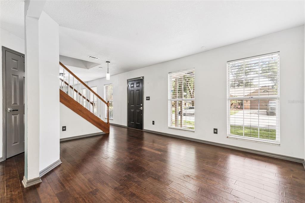 An empty living room features dark wood flooring, a staircase with wooden railings, and white walls — 440 BUCKSKIN COURT, WINTER SPRINGS, FL