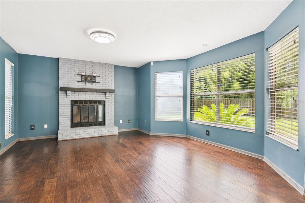 An empty living room features blue walls, a white brick fireplace, and dark wood flooring — 440 BUCKSKIN COURT, WINTER SPRINGS, FL