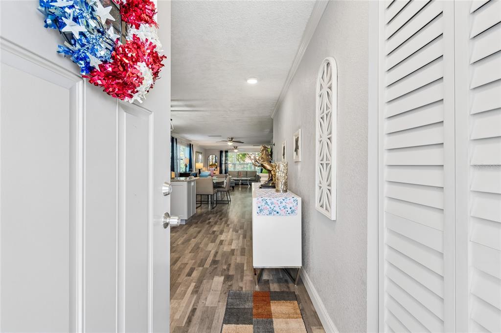 A view from an open front door into a home with wood-look flooring and furniture — 5501 80TH STREET N UNIT 102, ST PETERSBURG, FL