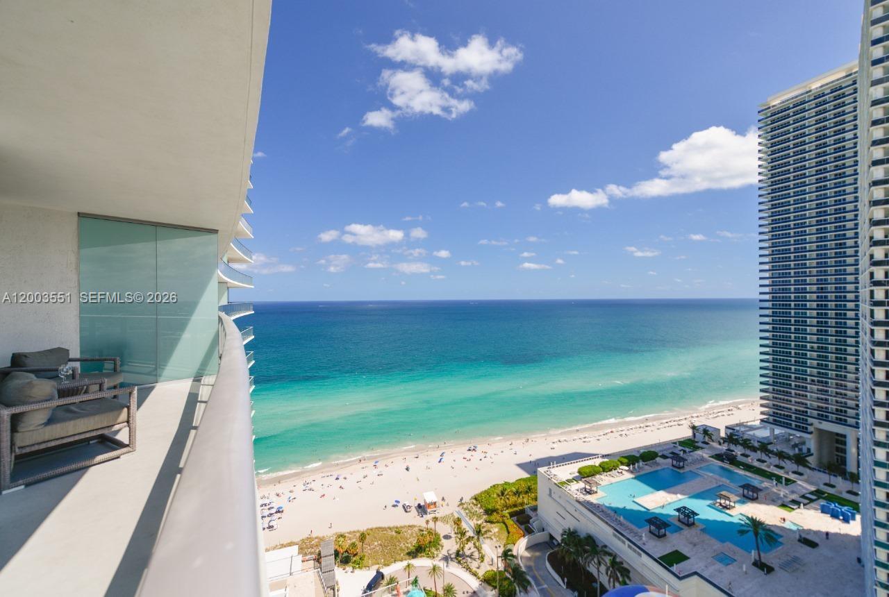A high-rise balcony overlooks a sandy beach, turquoise ocean, and a swimming pool deck — 4111 S Ocean Dr # 2207, Hollywood FL 33019, HOLLYWOOD, FL