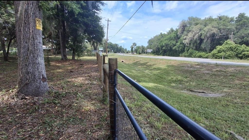 A view of a grassy roadside ditch next to a fenced property with trees — 5316 SW 13TH STREET, GAINESVILLE, FL
