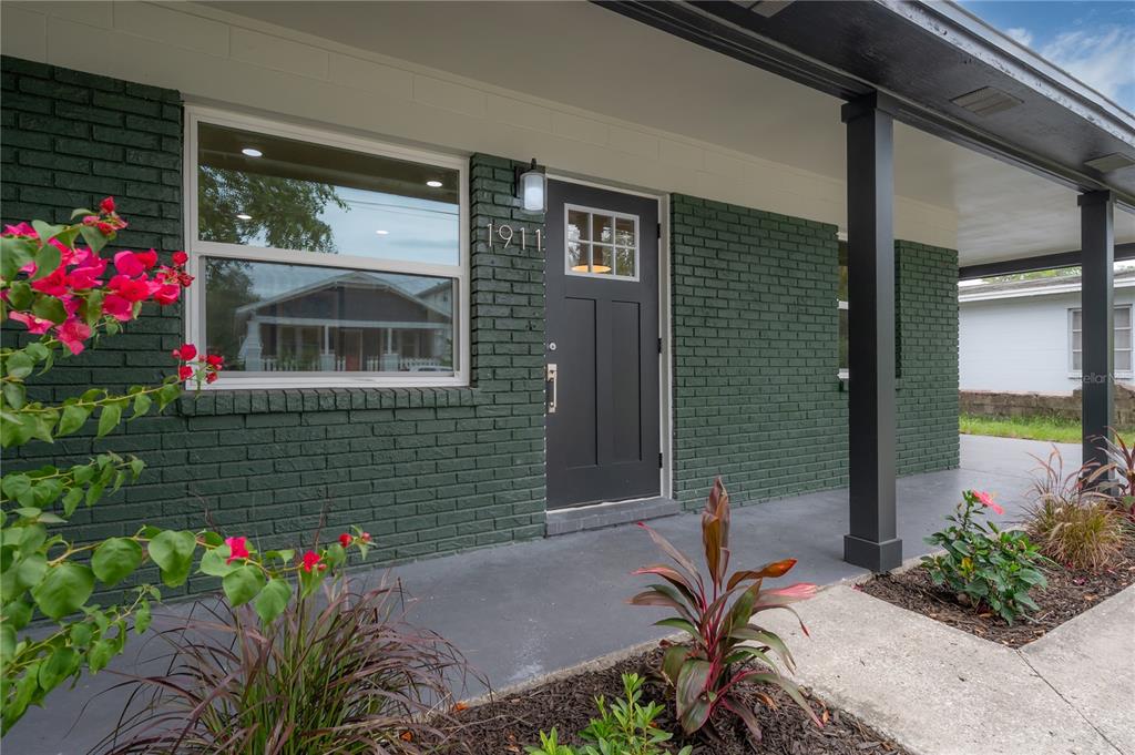 A dark green brick house exterior features a black front door and a covered porch — 1911 W CHERRY STREET, TAMPA, FL