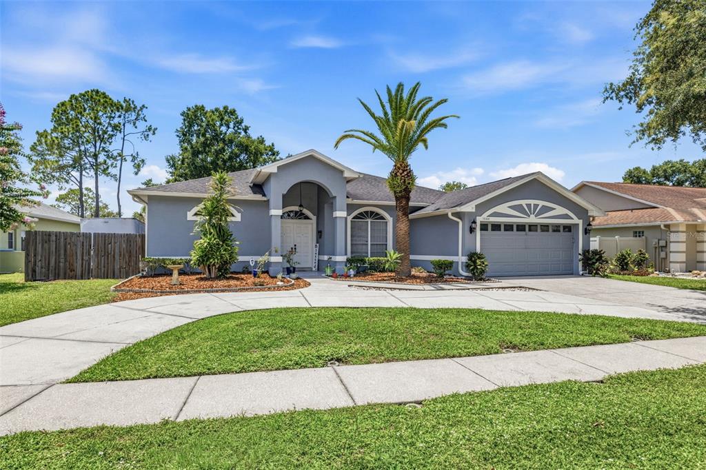 A single-story gray house with a palm tree, arched entryway, and a two-car garage — 15306 CARROLLTON LANE, TAMPA, FL