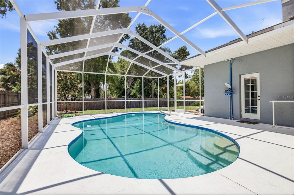 A backyard swimming pool is enclosed by a screened lanai next to a gray house — 15306 CARROLLTON LANE, TAMPA, FL