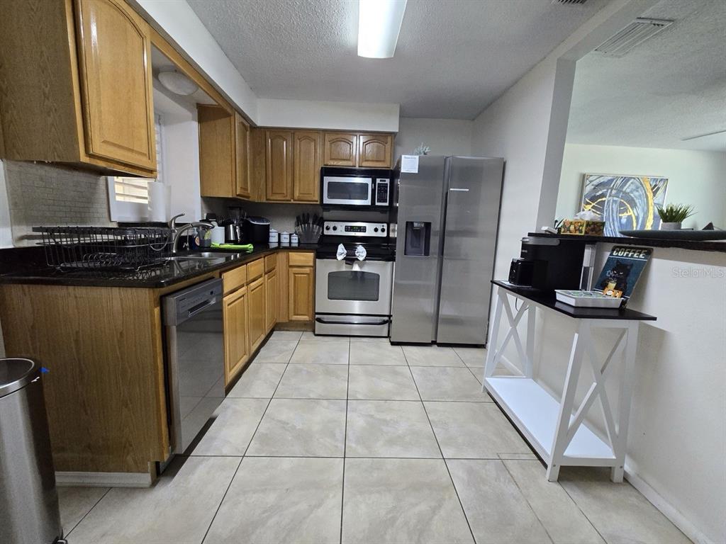 A kitchen features light wood cabinets, stainless steel appliances, and beige tile flooring — 1430 PARKVIEW LANE, LARGO, FL