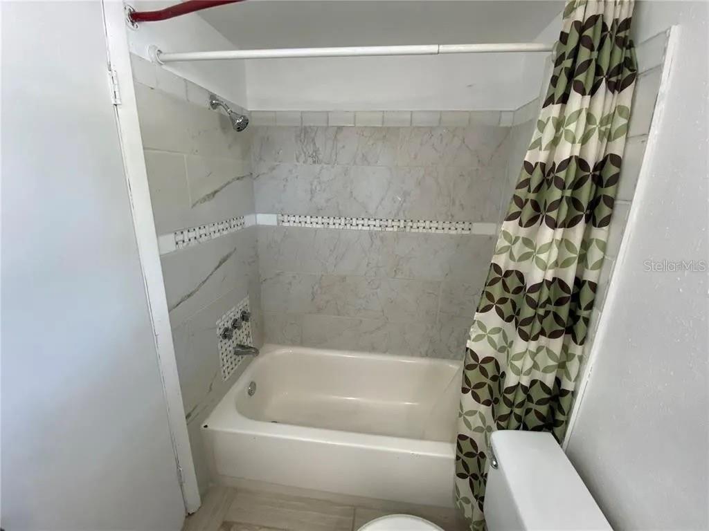 A bathroom features a white bathtub with marble-look tile walls and a patterned shower curtain — 1430 PARKVIEW LANE, LARGO, FL