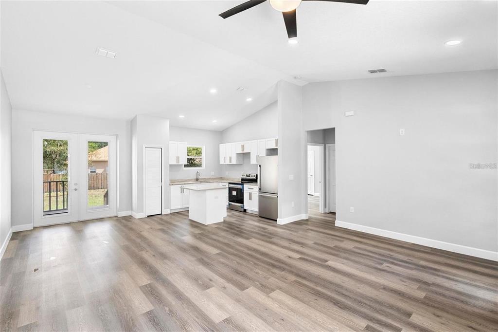 An open-concept kitchen and living area features light gray walls, wood-look flooring, and white cabinetry — 2379 8TH AVENUE, DELAND, FL