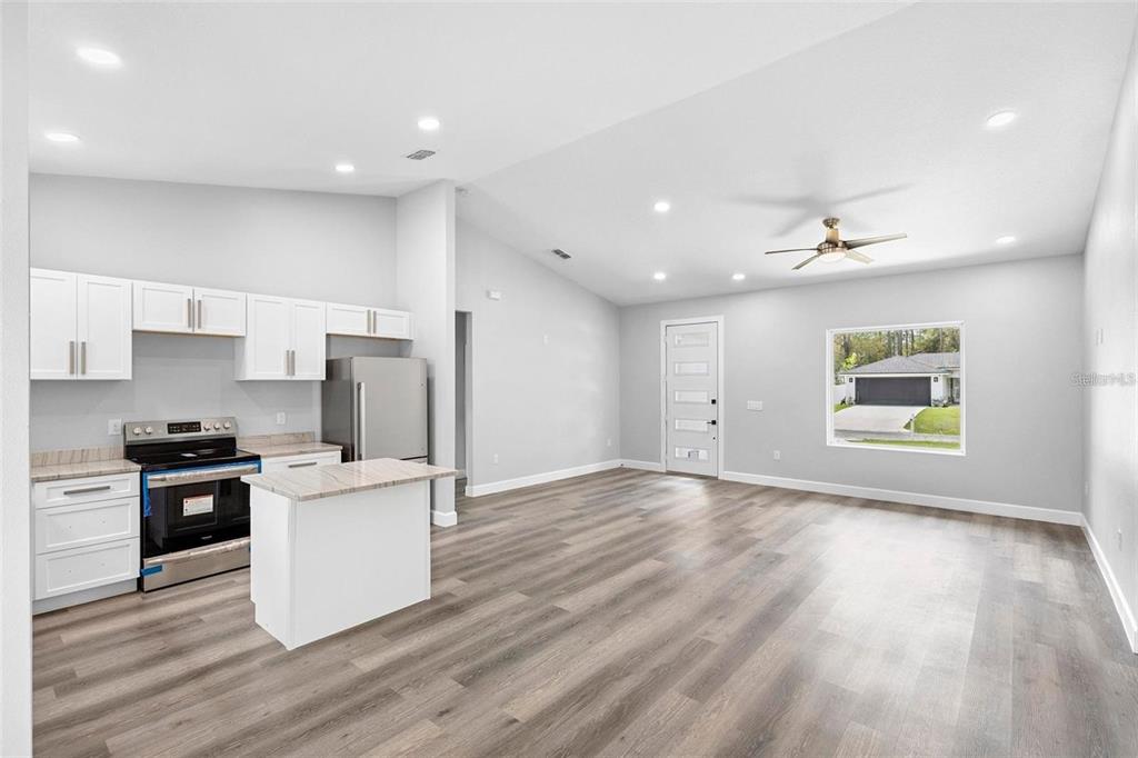 An open-concept kitchen and living area features white cabinets, stainless steel appliances, and wood flooring — 2379 8TH AVENUE, DELAND, FL