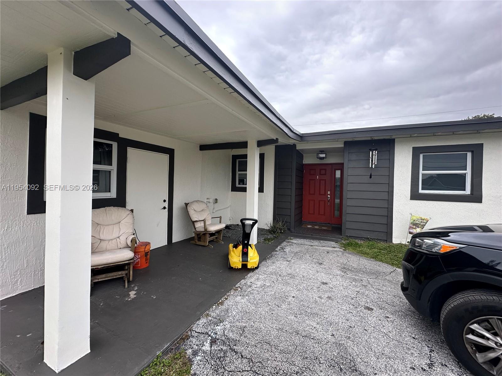 A covered porch with two chairs leads to a red front door on a house — 5700 SW 54th Ter, Davie FL 33314, DAVIE, FL