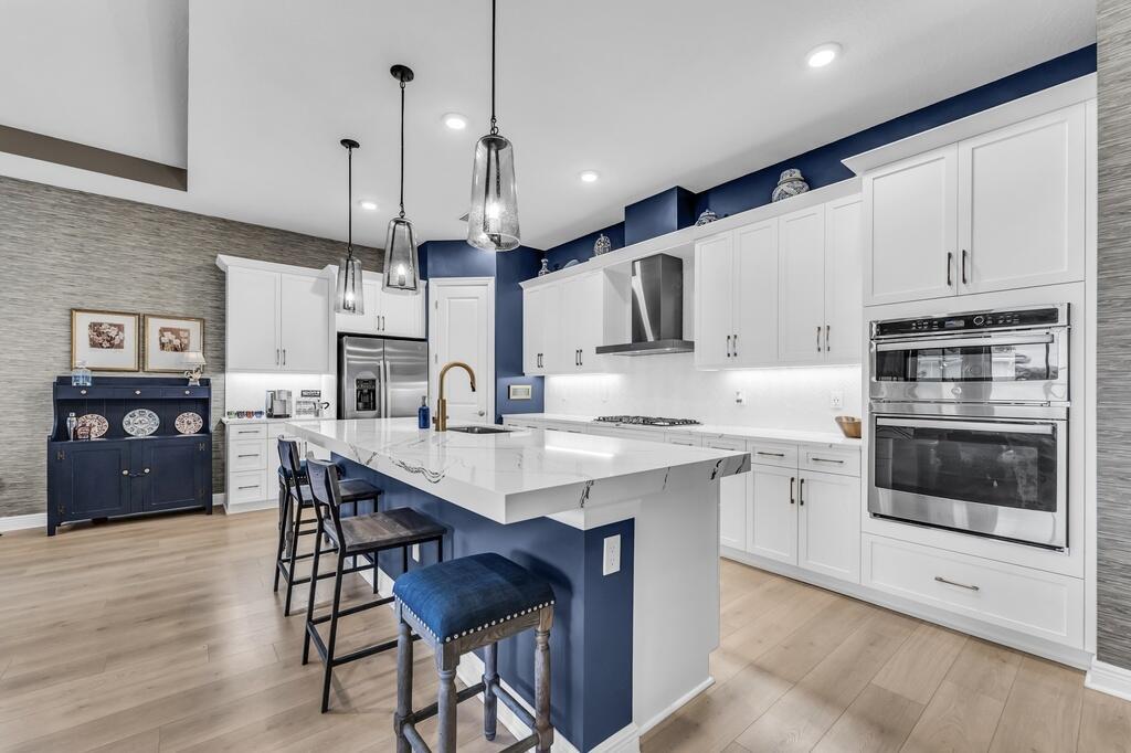 A modern kitchen features white cabinetry, a navy blue island with bar stools, and stainless appliances — 15665 Merritt Drive, Westlake FL 33470, WESTLAKE, FL