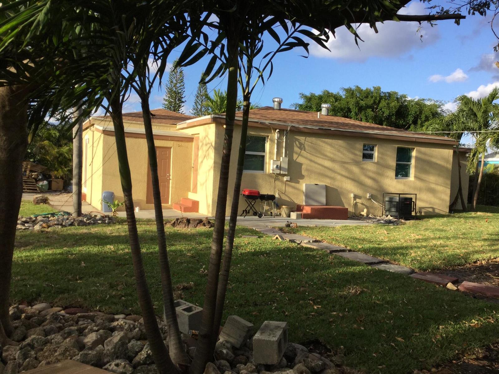 A yellow stucco house with a brown roof, palm trees, and a backyard patio area — 130 NW 5th Avenue, Boynton Beach FL 33435, BOYNTON BEACH, FL