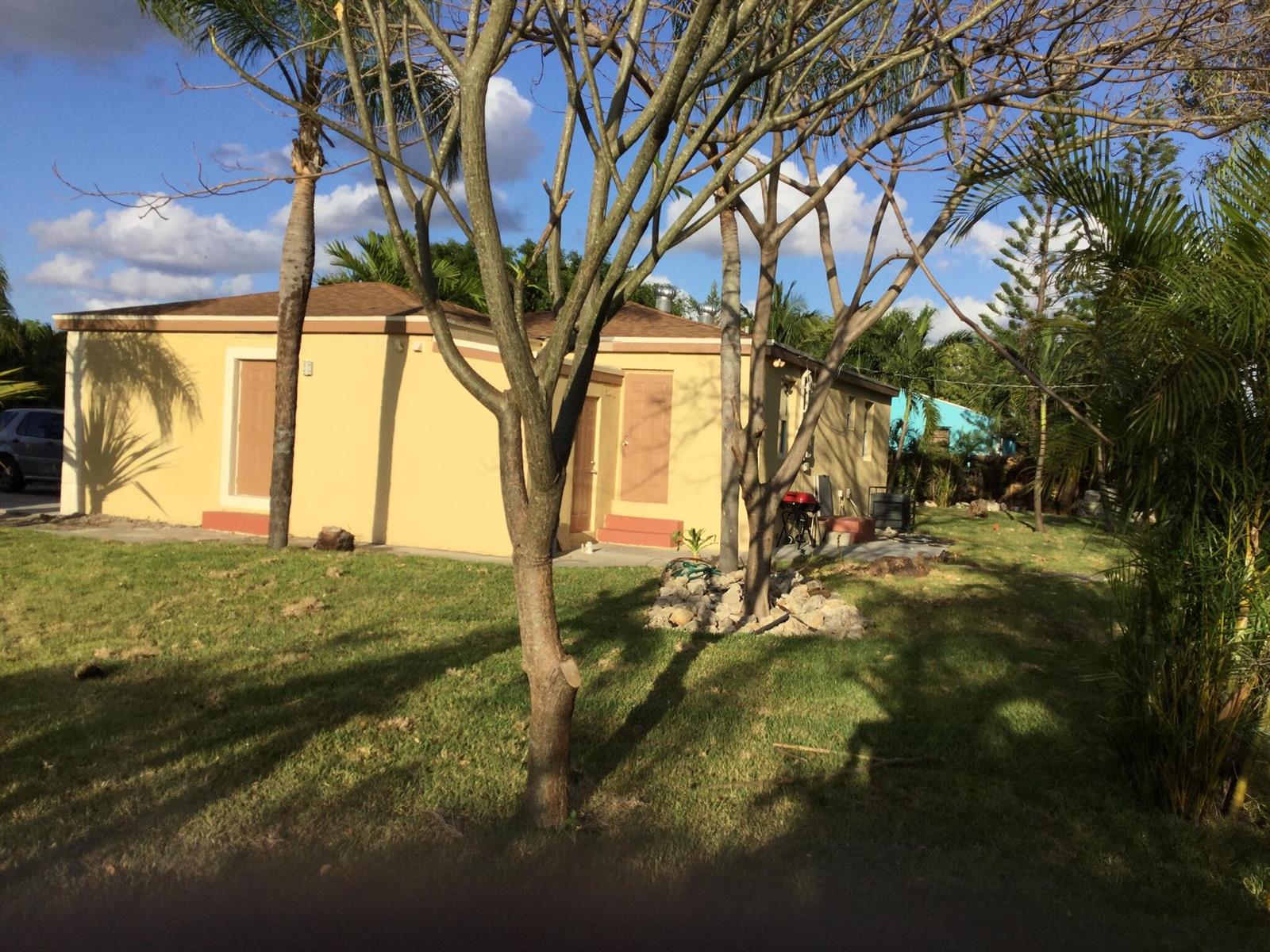 A yellow single-story house with two doors stands on a grassy lot with several trees — 130 NW 5th Avenue, Boynton Beach FL 33435, BOYNTON BEACH, FL