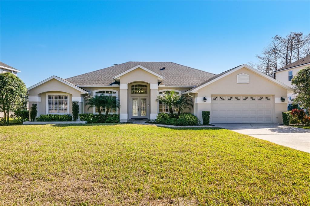 A single-story suburban house with a beige stucco exterior, a two-car garage, and a lawn — 655 CALEDONIA PLACE, SANFORD, FL