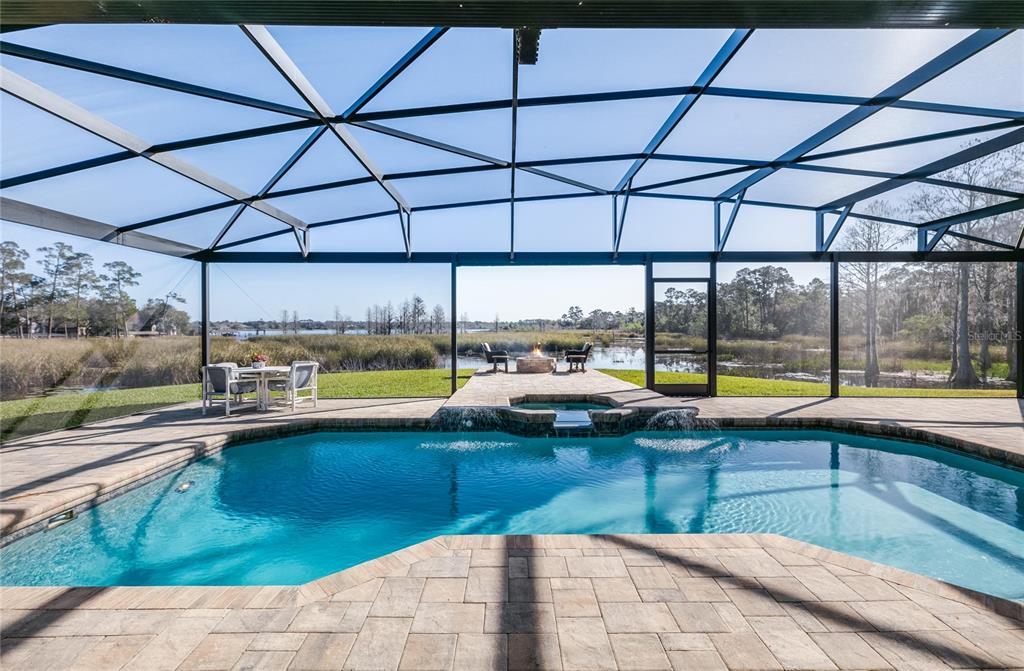 A screened-in pool patio features a hot tub, fire pit, and views of a lake — 655 CALEDONIA PLACE, SANFORD, FL
