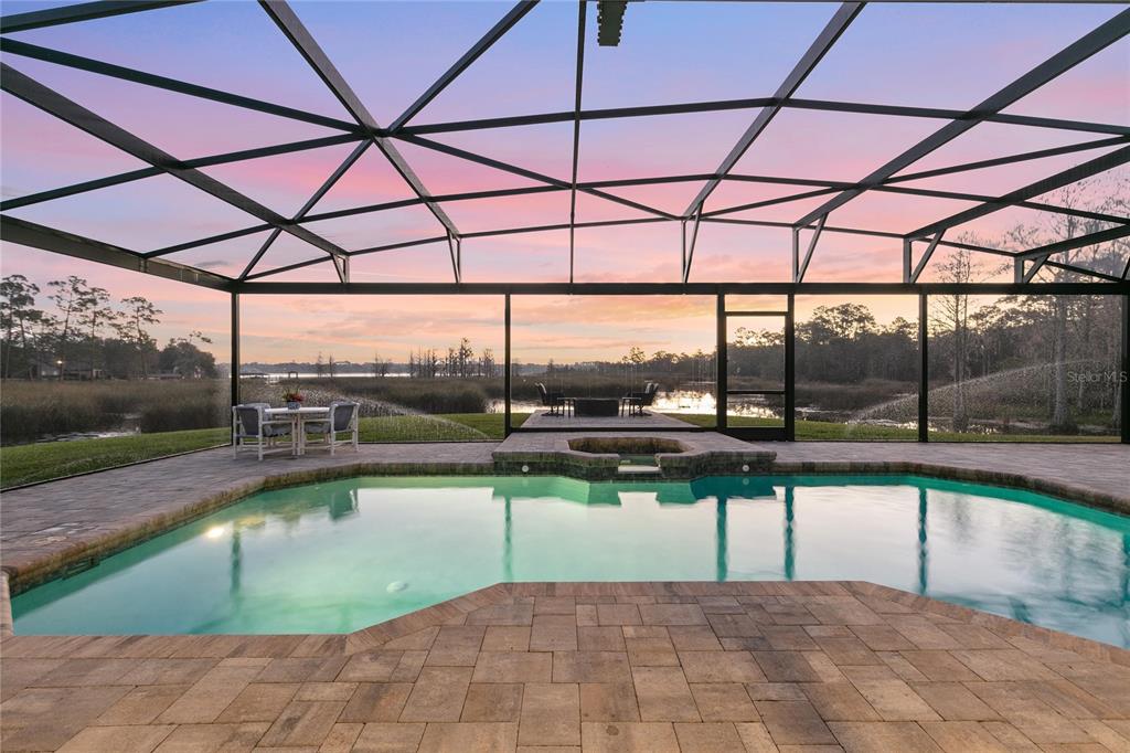 A screened-in pool patio overlooks a lake at sunset with a built-in spa and pavers — 655 CALEDONIA PLACE, SANFORD, FL