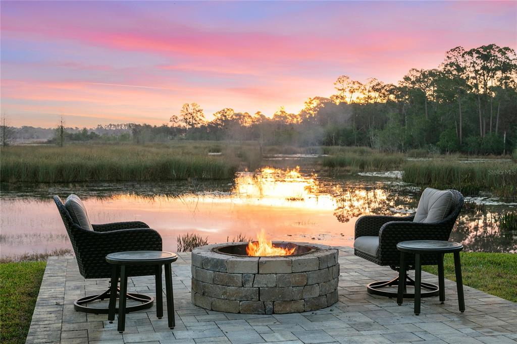A stone fire pit and two chairs sit on a patio overlooking a marshy pond — 655 CALEDONIA PLACE, SANFORD, FL