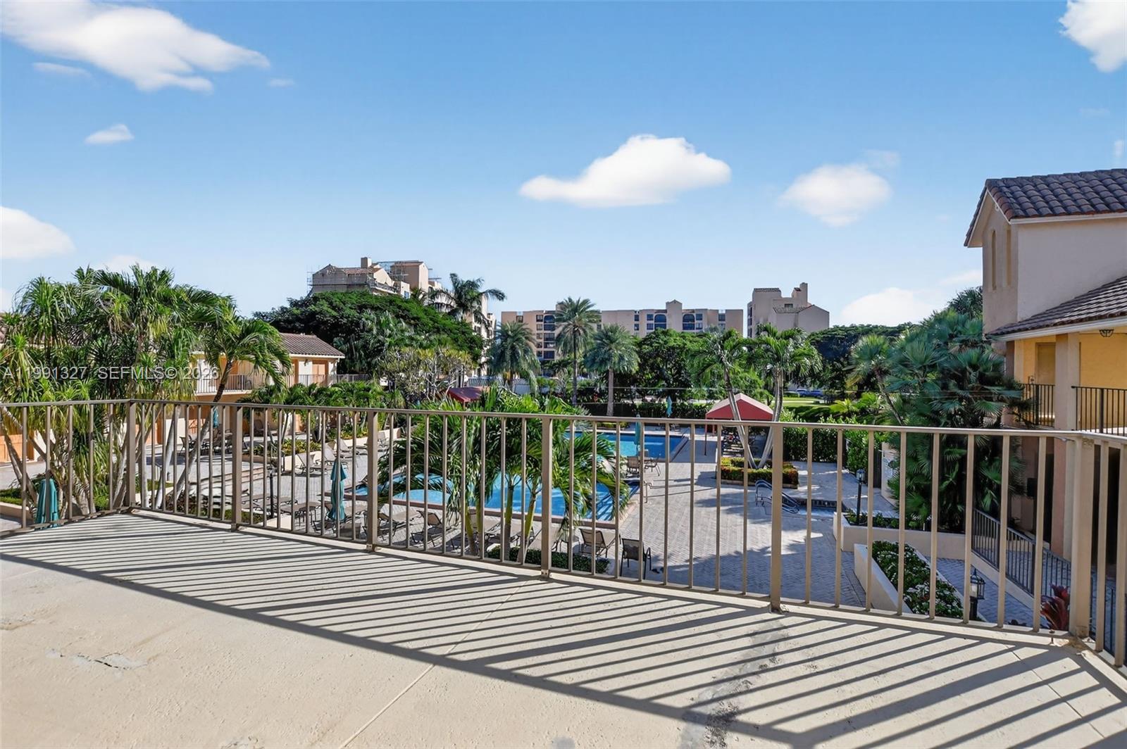A balcony overlooks a swimming pool area surrounded by palm trees and apartment buildings — 7145 Promenade Dr # 702, Boca Raton FL 33433, BOCA RATON, FL