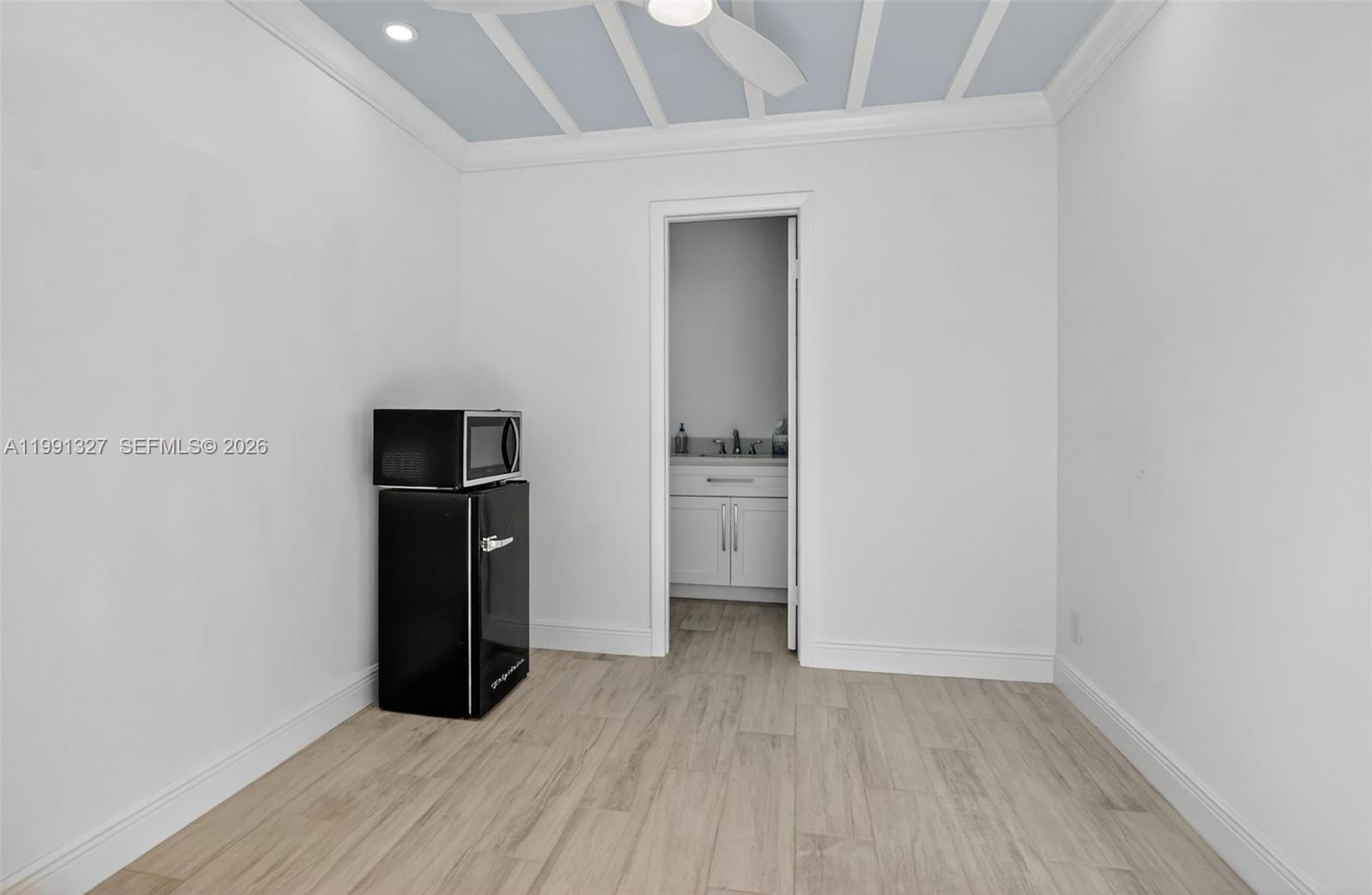 A small room features light wood-look flooring, a black mini-fridge, and an attached bathroom — 7145 Promenade Dr # 702, Boca Raton FL 33433, BOCA RATON, FL
