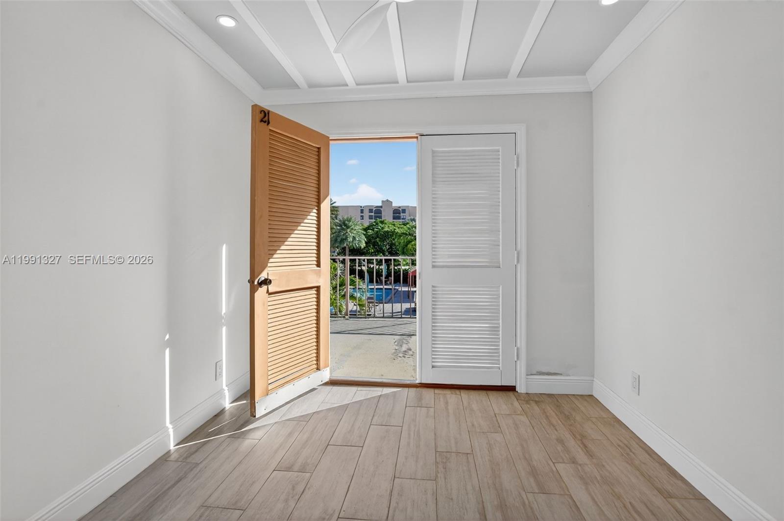 A room with light wood-look flooring features a louvered door opening to a balcony — 7145 Promenade Dr # 702, Boca Raton FL 33433, BOCA RATON, FL